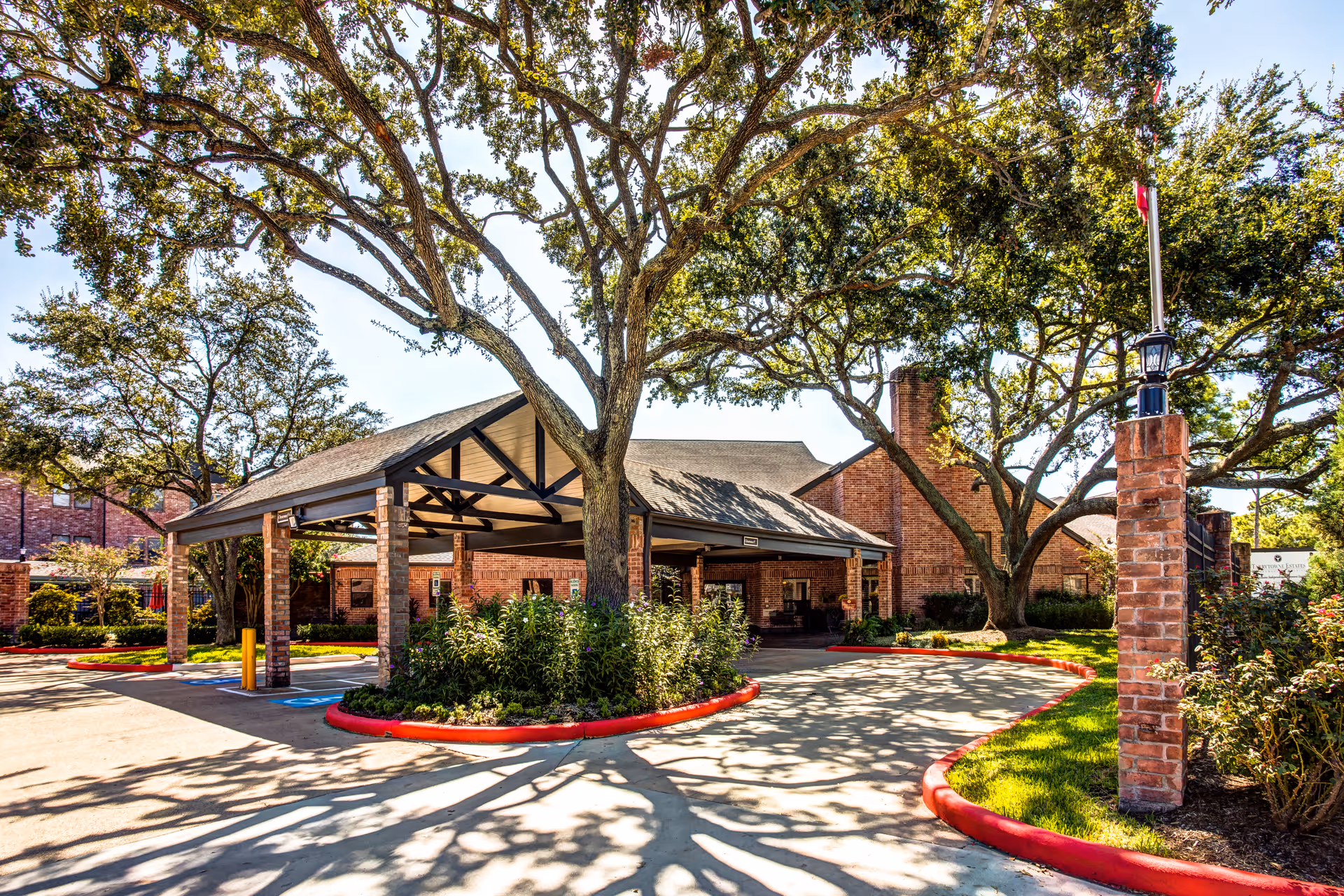 Covered entrance to a senior living facility with brick, trees, and landscaped grounds.