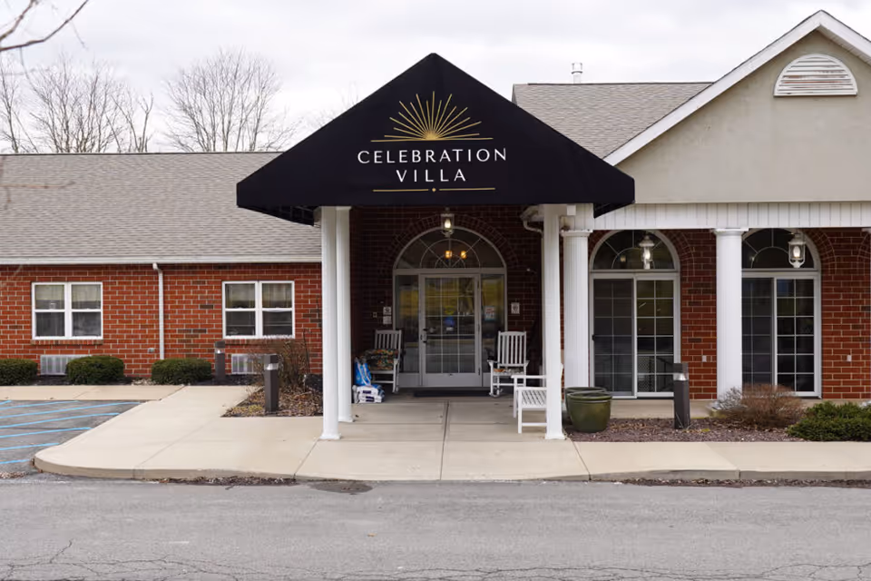 Front entrance of Celebration Villa with a black awning, white columns, rocking chairs, and a red brick facade.