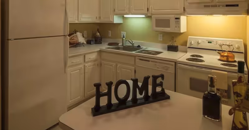 Compact kitchen with white cabinets and appliances and a countertop decoration spelling 'HOME'.
