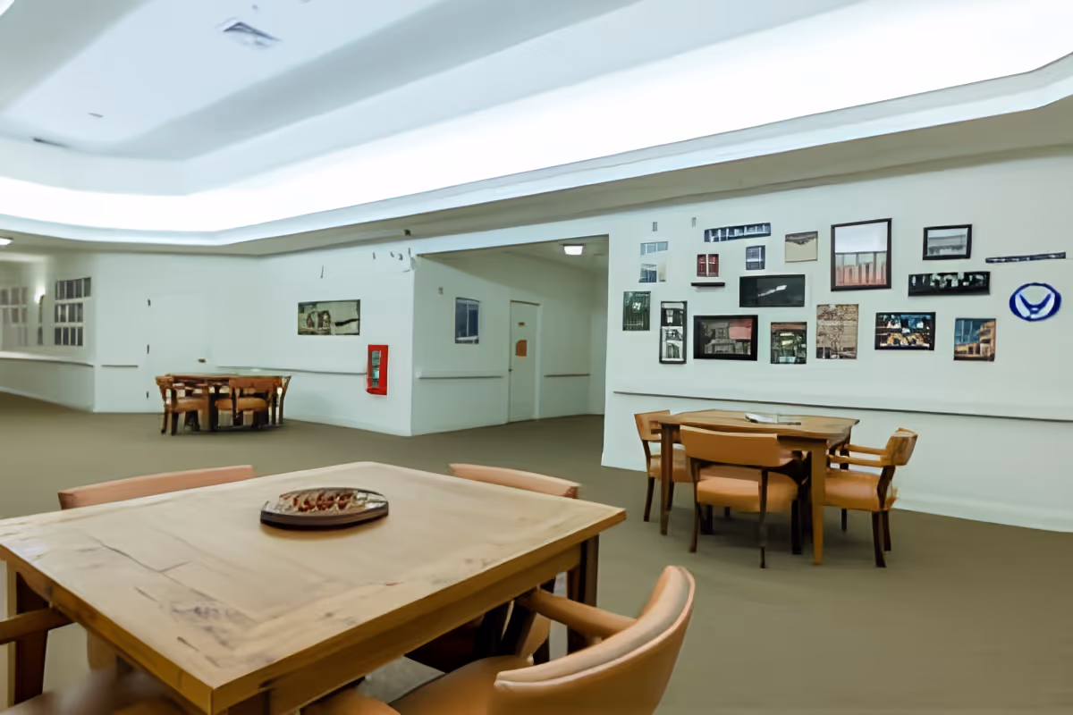 Large bright communal dining area with wooden tables and chairs and a gallery wall of framed pictures.
