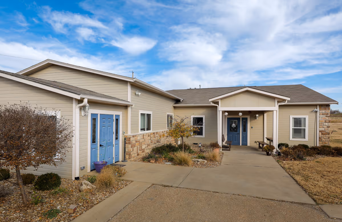 Single-story beige building front with stone accents, landscaping and blue entry doors under a covered porch.