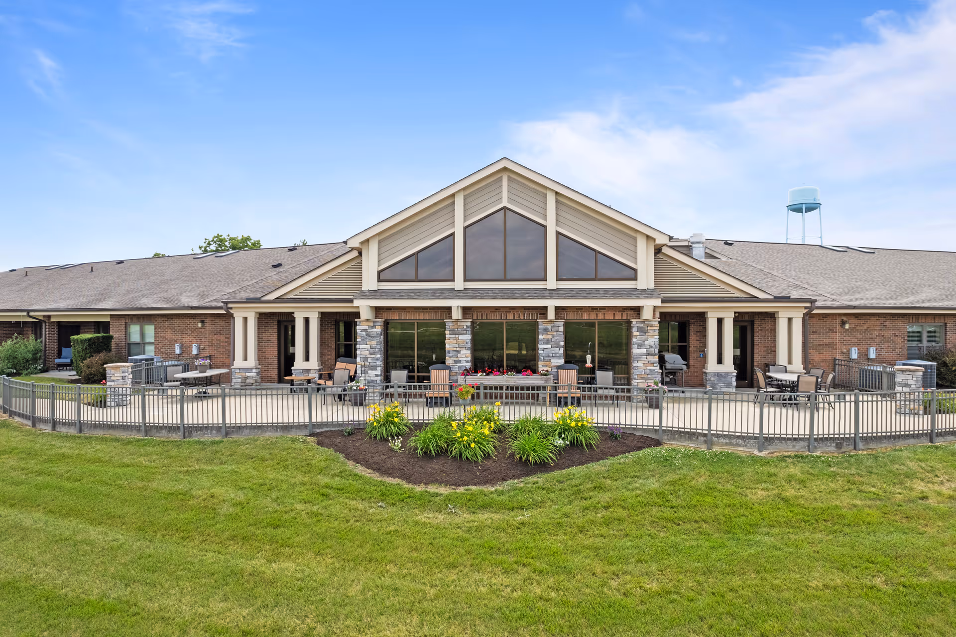 Front exterior of a single-story brick nursing facility with a covered patio, large triangular windows, outdoor seating, and a manicured lawn.