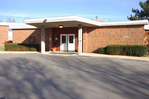Entrance of a brick senior living facility with a covered portico and two doors.