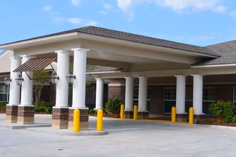 Covered driveway entrance with white columns, brick base, and yellow bollards at Magnolia Manor.