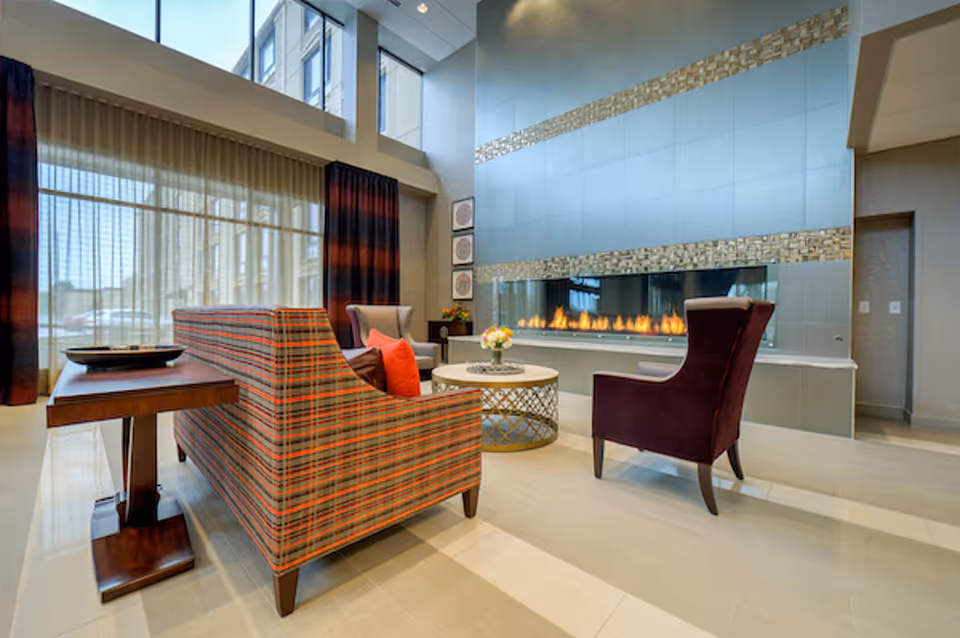 A modern lounge with patterned sofas and armchairs around a round coffee table and a long linear fireplace beneath tall windows.