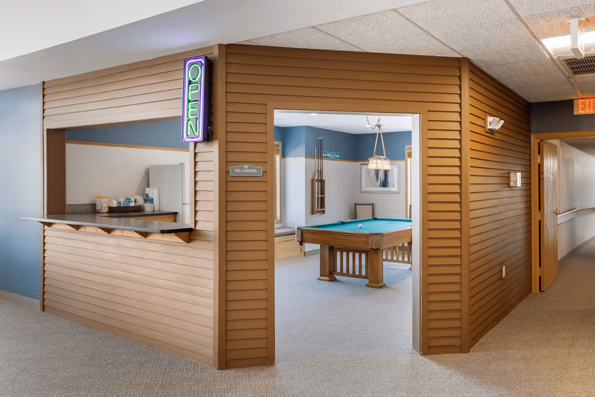 Interior recreation area showing a billiards room with a pool table and a serving window with a neon "OPEN" sign.