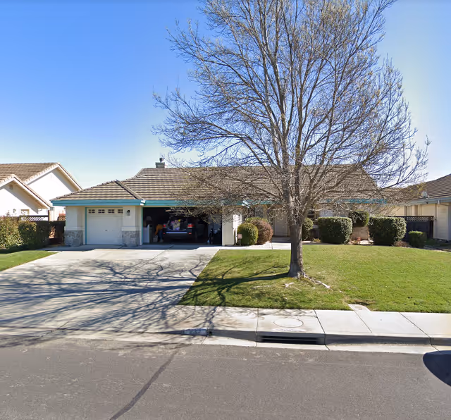 Single-story suburban home with an open two-car garage, a leafless tree on the front lawn, and a concrete driveway.