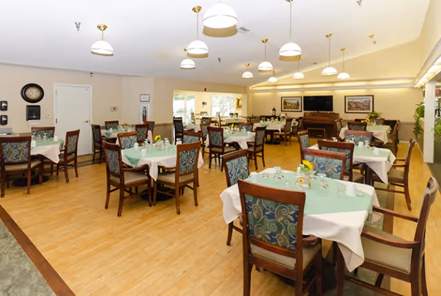 Spacious dining room with multiple tables set with green tablecloths and wooden chairs under pendant lights.