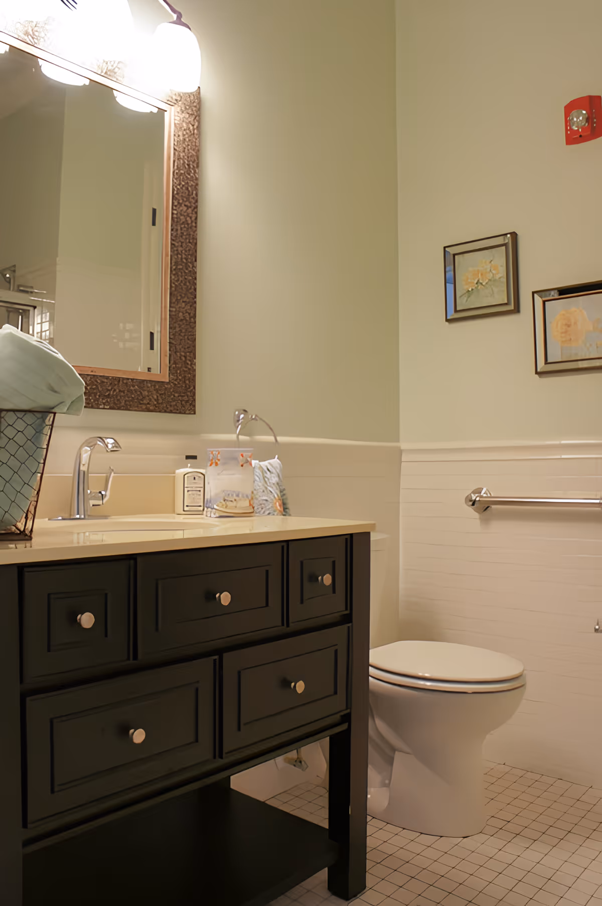Bathroom featuring a dark wood vanity with sink and mirror, a toilet with a grab bar, and framed wall art on a pale green wall.