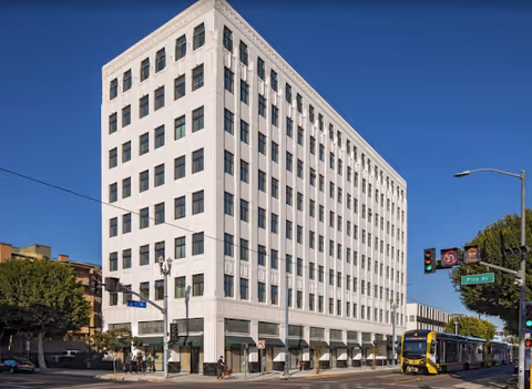 Tall white multi-story building on a busy street with a bus in front.