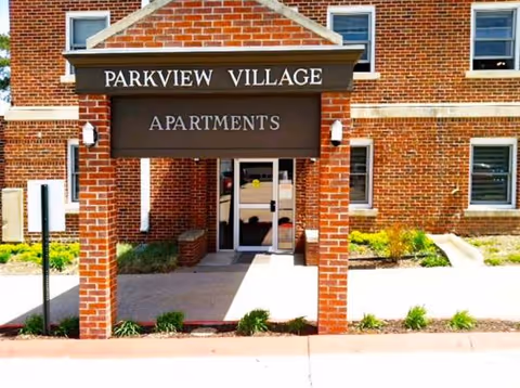 Brick building entrance with a covered canopy and Parkview Village Apartments sign.