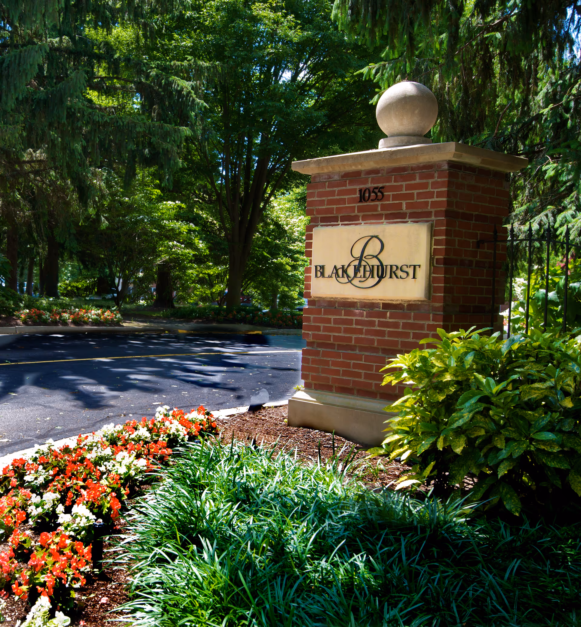 Brick entrance pillar with a 'Blakehurst' sign surrounded by landscaped flowers and trees.