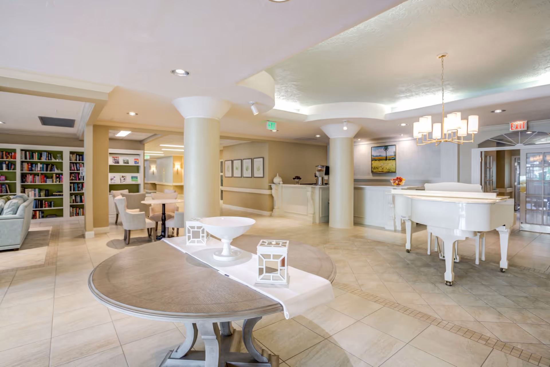 Bright, elegant senior living facility lobby with a round table centerpiece, white grand piano, seating area and bookshelf.
