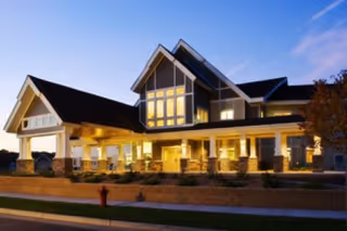 Well-lit front exterior of a multi-story assisted living facility with a covered entrance and large windows at dusk.