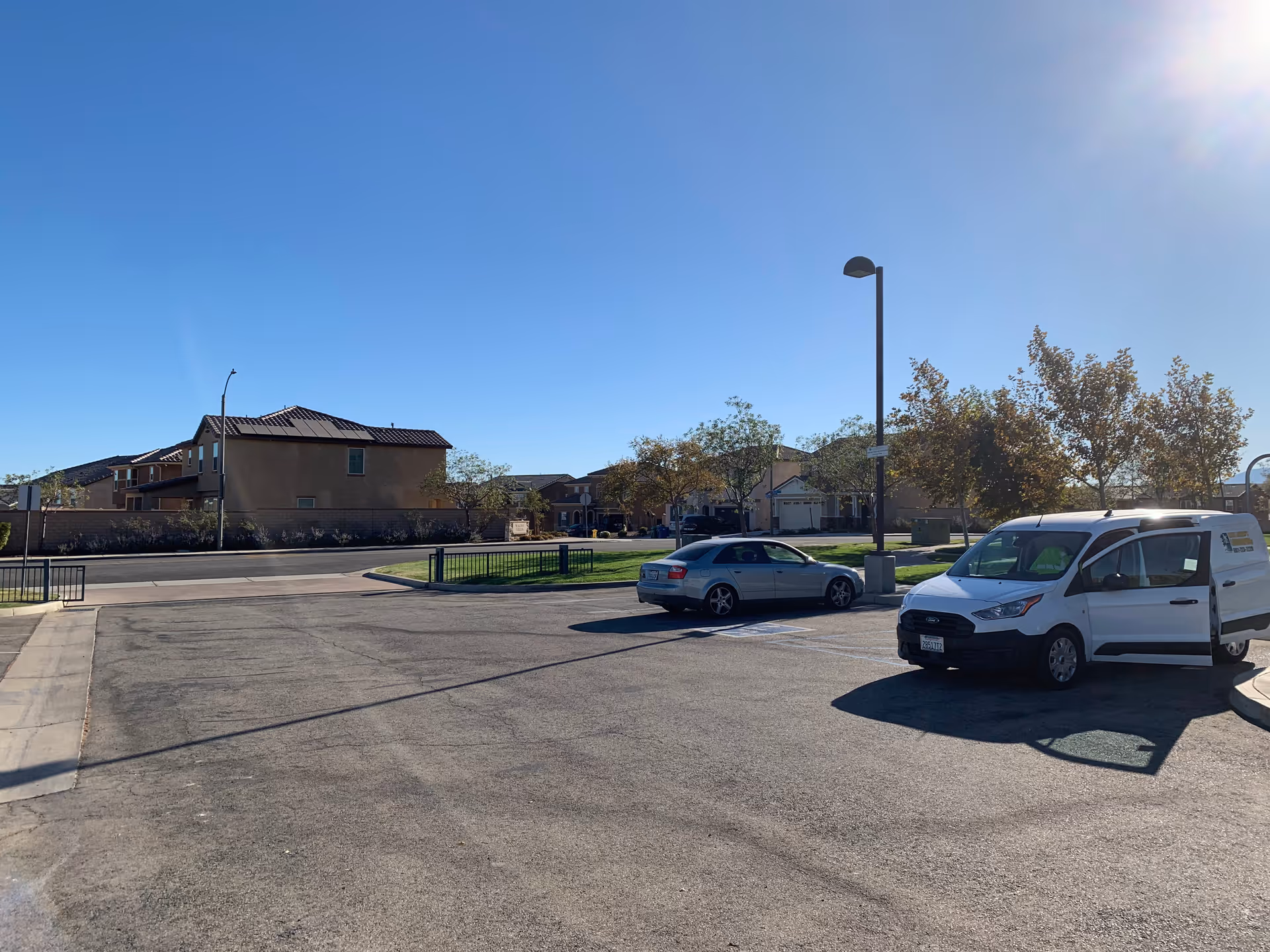 Parking lot with a white van and a silver car in front of residential buildings under a clear blue sky.