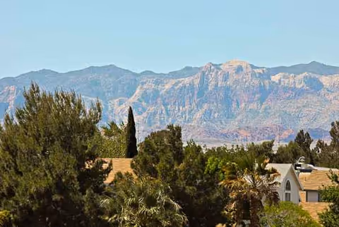 Exterior landscape showing mountains behind trees and rooftops in the foreground.