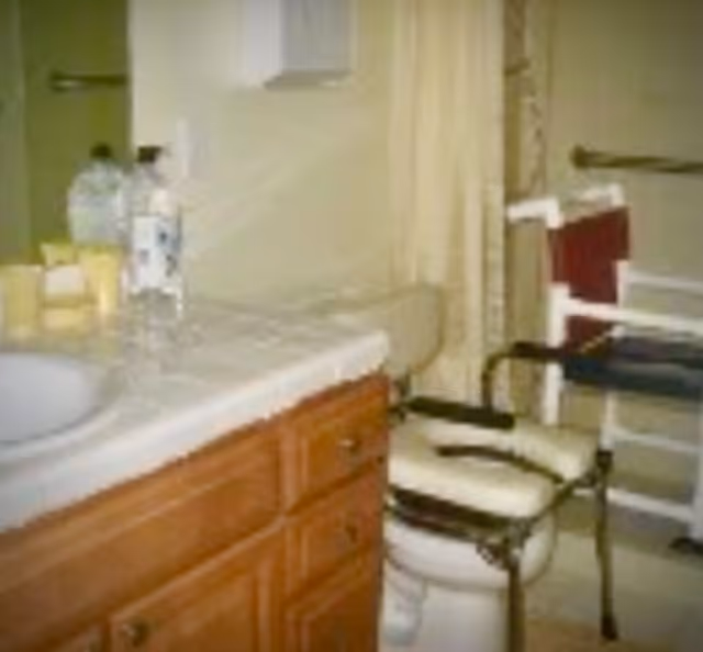 Small bathroom with wooden cabinet, countertop sink, and a chair beside a walker.
