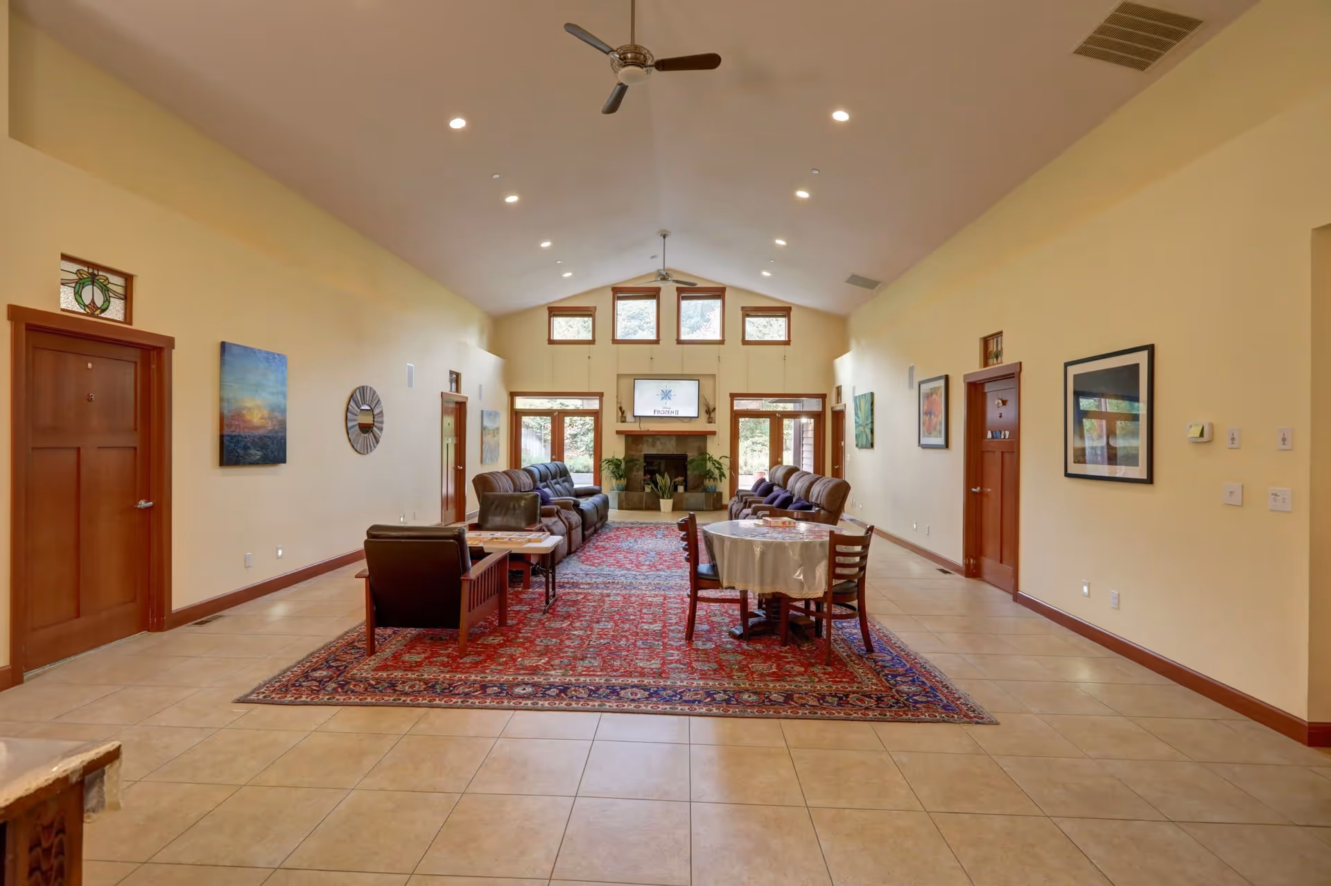 Spacious communal living room with sofas, chairs, a dining table on a large area rug and a fireplace under a vaulted ceiling.