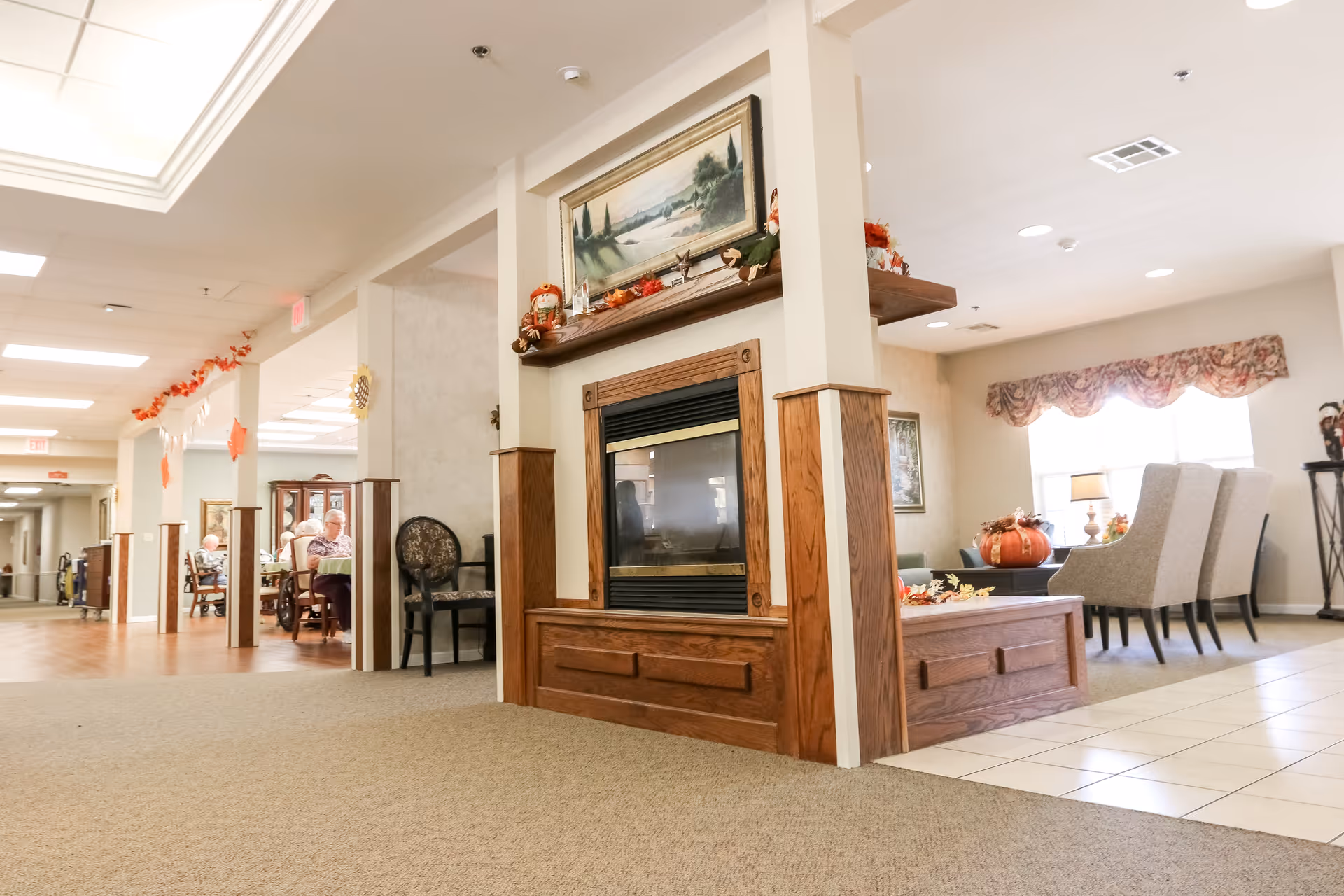 Bright communal living area with a central wood-framed fireplace, seating and dining tables in the background.