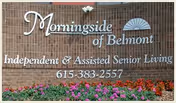 Brick wall sign for Morningside of Belmont with text indicating Independent & Assisted Senior Living and a phone number 615-383-2557, surrounded by colorful flowers at the base.
