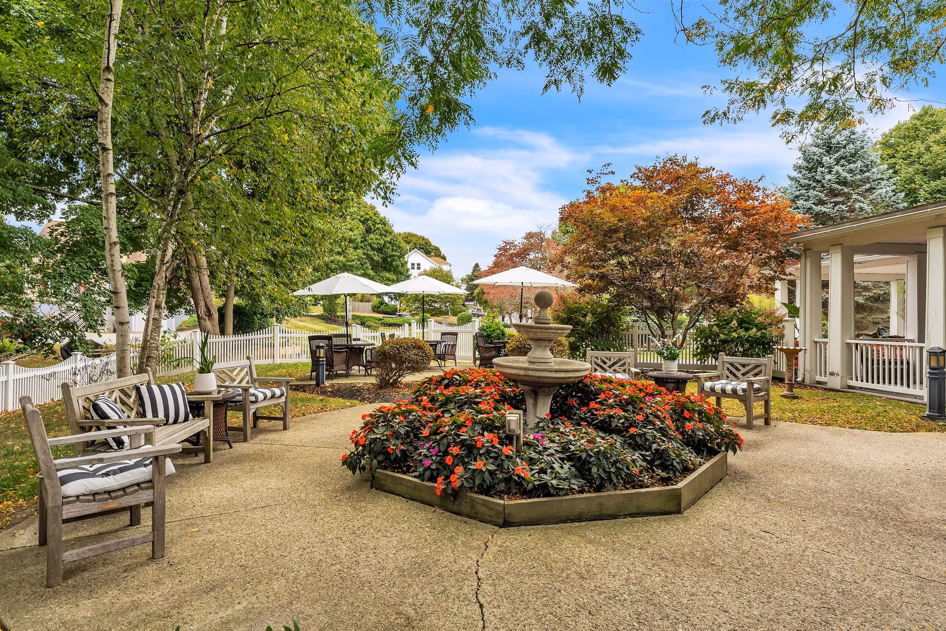 Landscaped courtyard with a central fountain, colorful flowerbeds, benches, and patio tables with umbrellas.