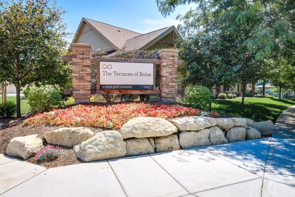 Entrance sign reading 'The Terraces of Boise' set among landscaped flowers, large rocks and trees in front of the building.