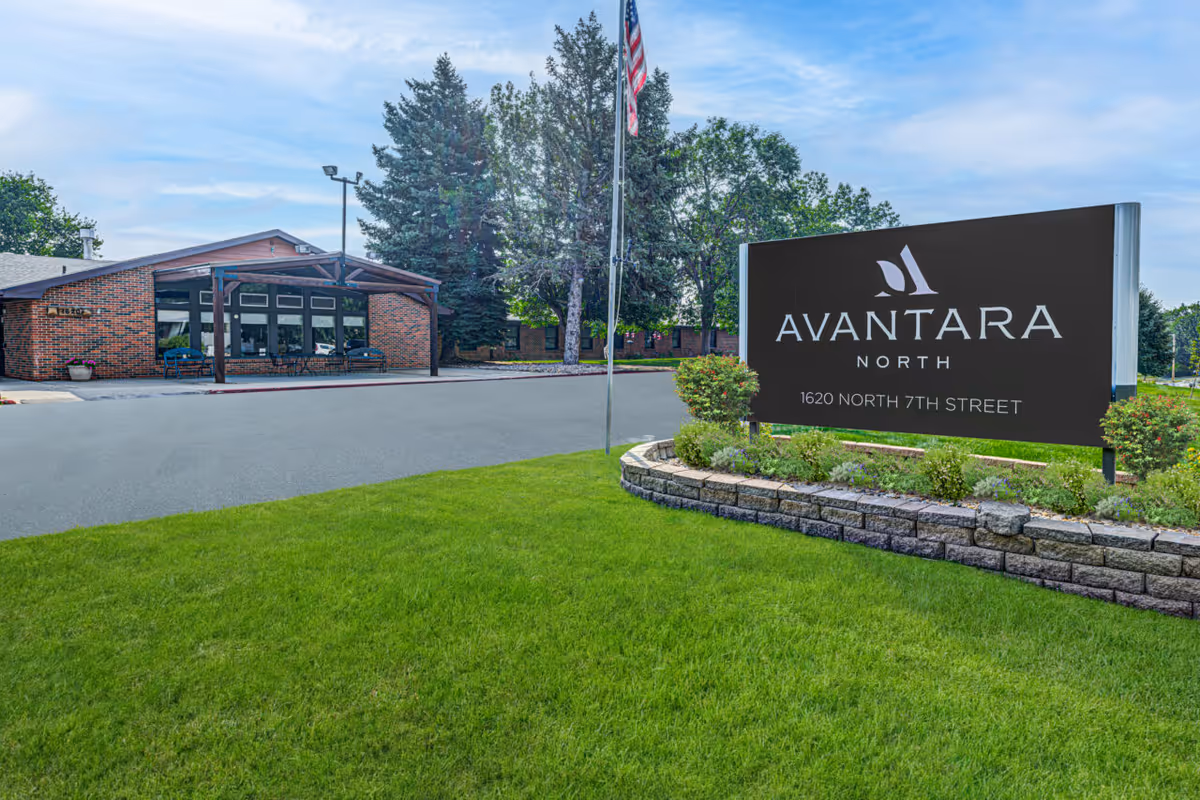 Exterior view of Avantara North facility with a brick building, large sign, flagpole, and manicured lawn.