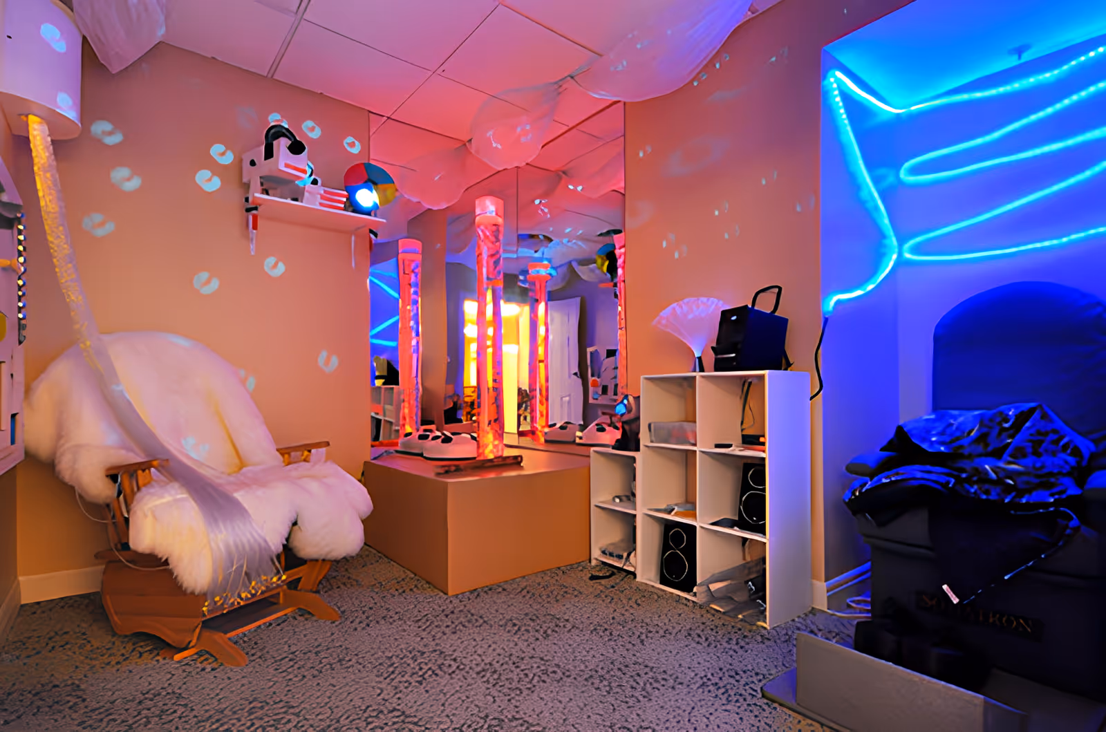 Sensory therapy room with a fur-covered rocking chair, glowing bubble tubes and colorful LED lighting.