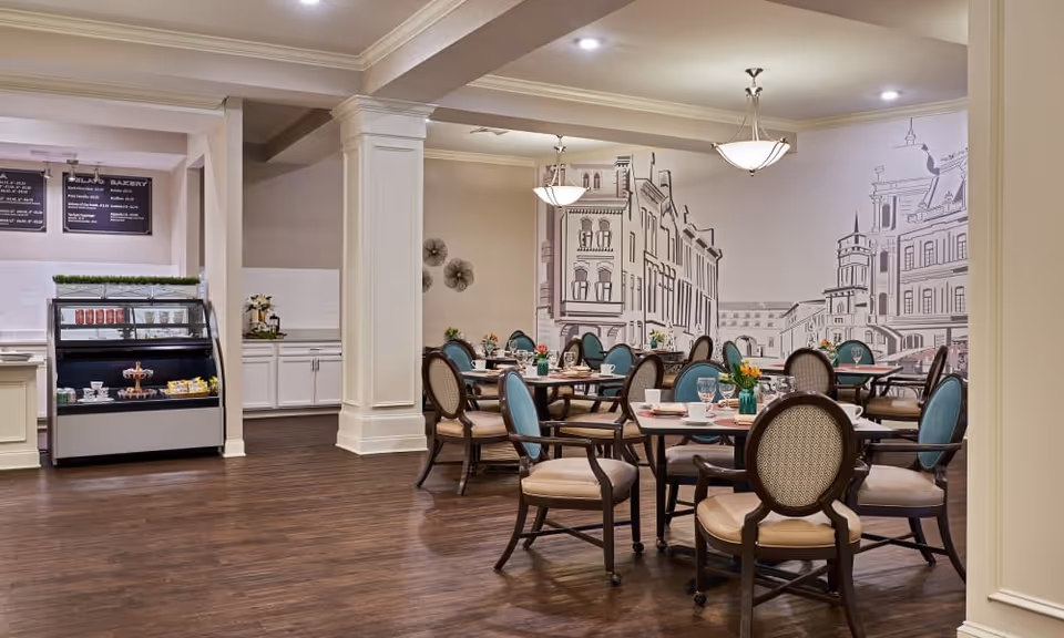 Dining room with round tables set for meals, upholstered chairs, a muraled wall, and a small service counter.