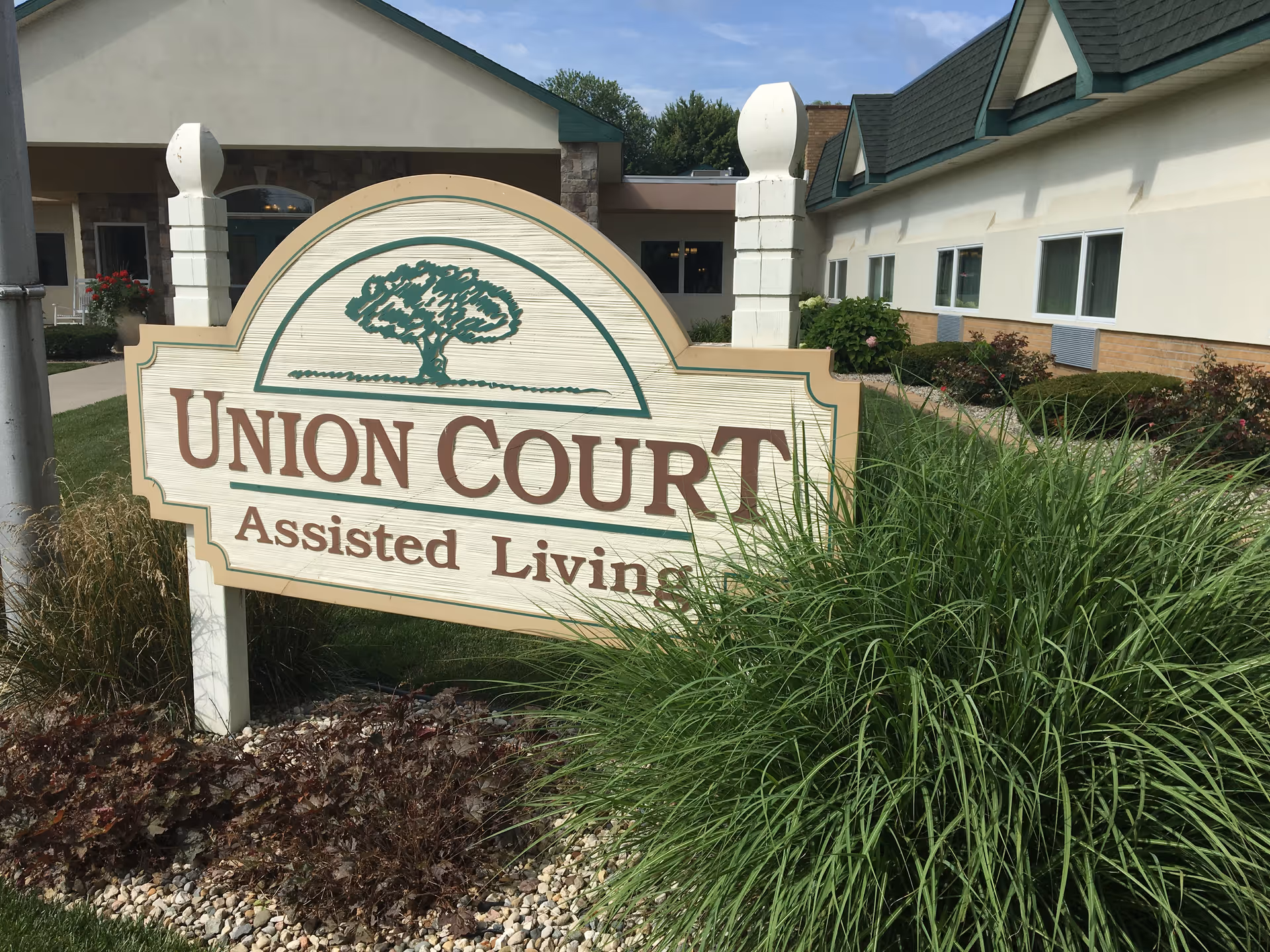 Wooden sign reading "Union Court Assisted Living" stands in landscaped grounds in front of the facility building.
