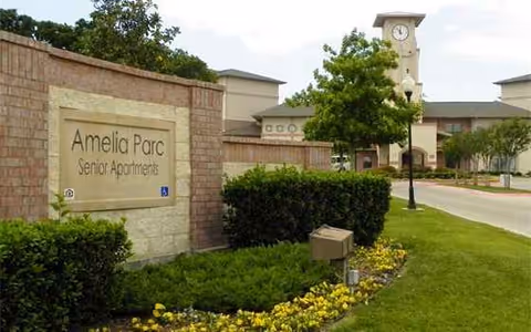 Exterior view of Amelia Parc Senior Apartments entrance with sign, shrubs, and clock tower.