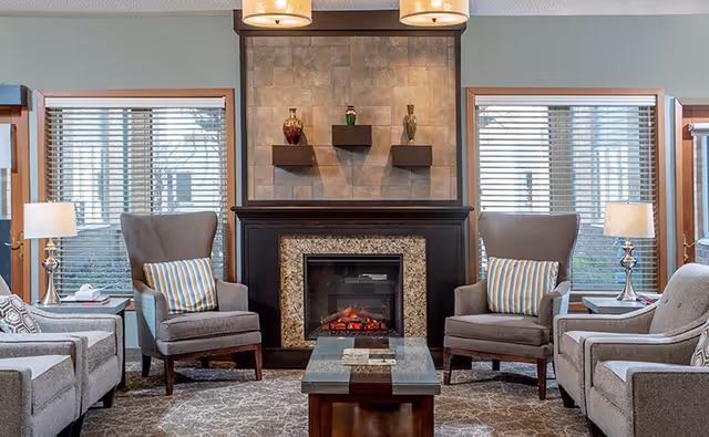 Cozy living room with a central fireplace flanked by two wingback chairs, sofas, a coffee table and decorative shelving.