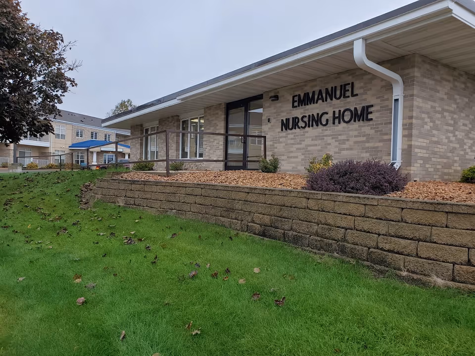 Front exterior of the Emmanuel Nursing Home building with brick facade, entrance and a sloped grassy lawn.