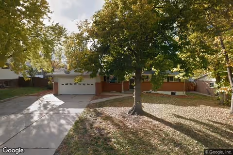 Front exterior view of a single-story residential building with a two-car garage, surrounded by trees with autumn foliage and a lawn covered in fallen leaves.