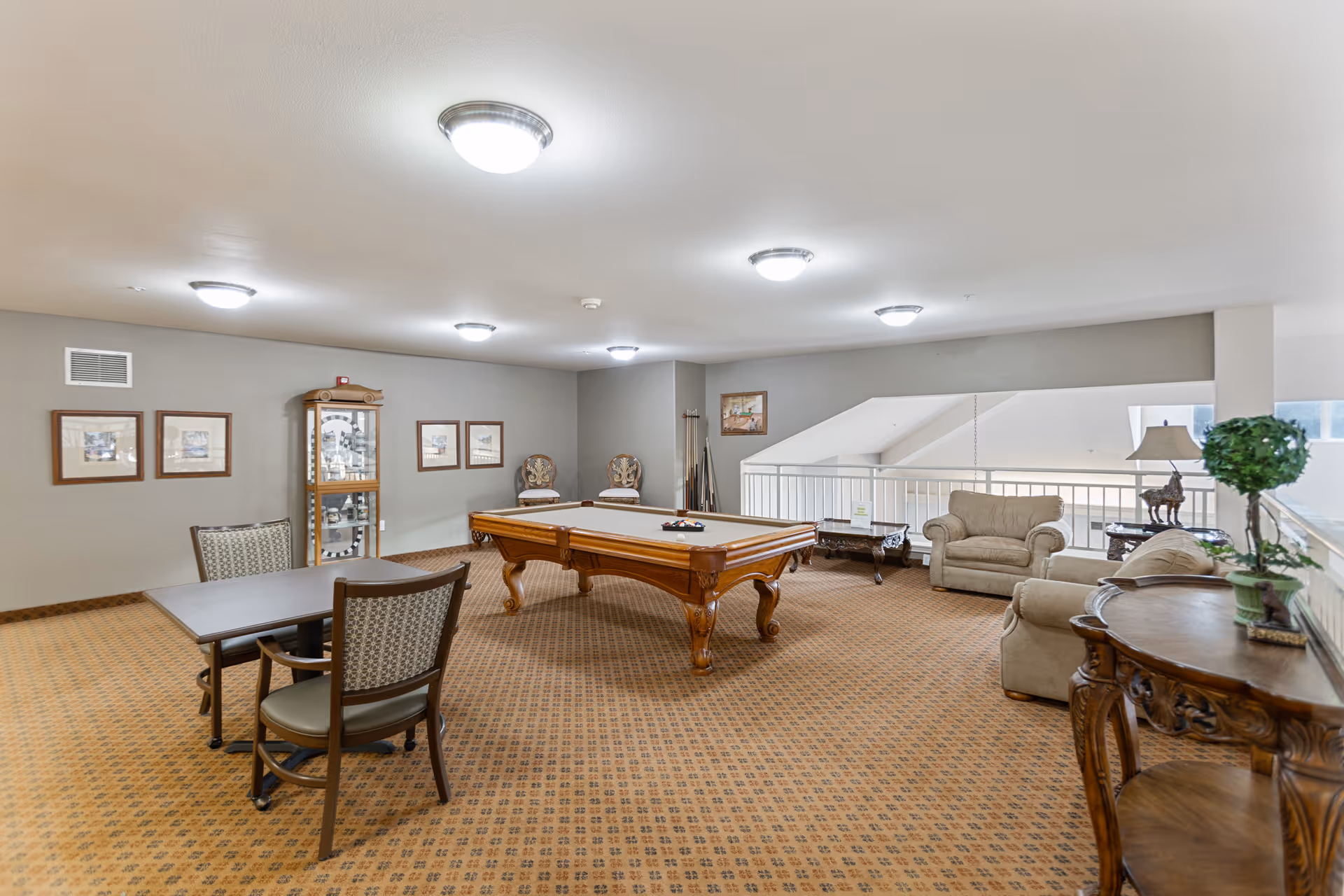 Spacious senior living common room featuring a pool table, seating area, tables, and decorative furnishings.