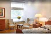 A furnished bedroom with a bed, nightstand and lamp, two armchairs by a window with a small table and a dresser.