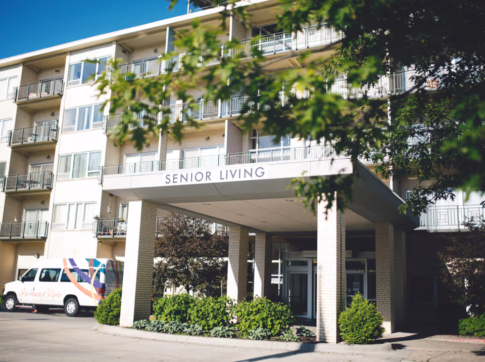 Entrance of a multi-story senior living building with a covered drop-off labeled "Senior Living" and a facility van parked nearby.