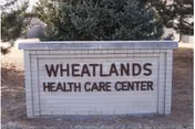 Low brick monument sign reading "WHEATLANDS HEALTH CARE CENTER" with trees behind it.
