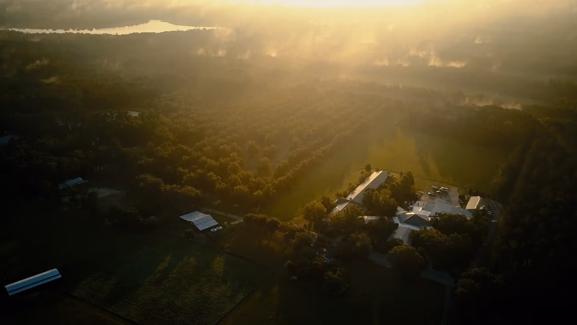 Aerial view of a small senior living campus and nearby buildings surrounded by trees and fields in warm morning light.