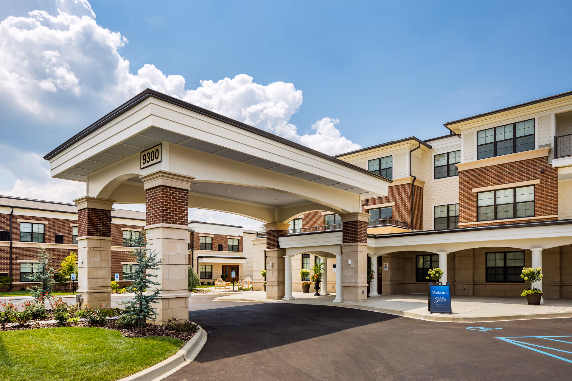 Exterior view of The Grand Senior Living entrance with brick columns and covered drop-off.