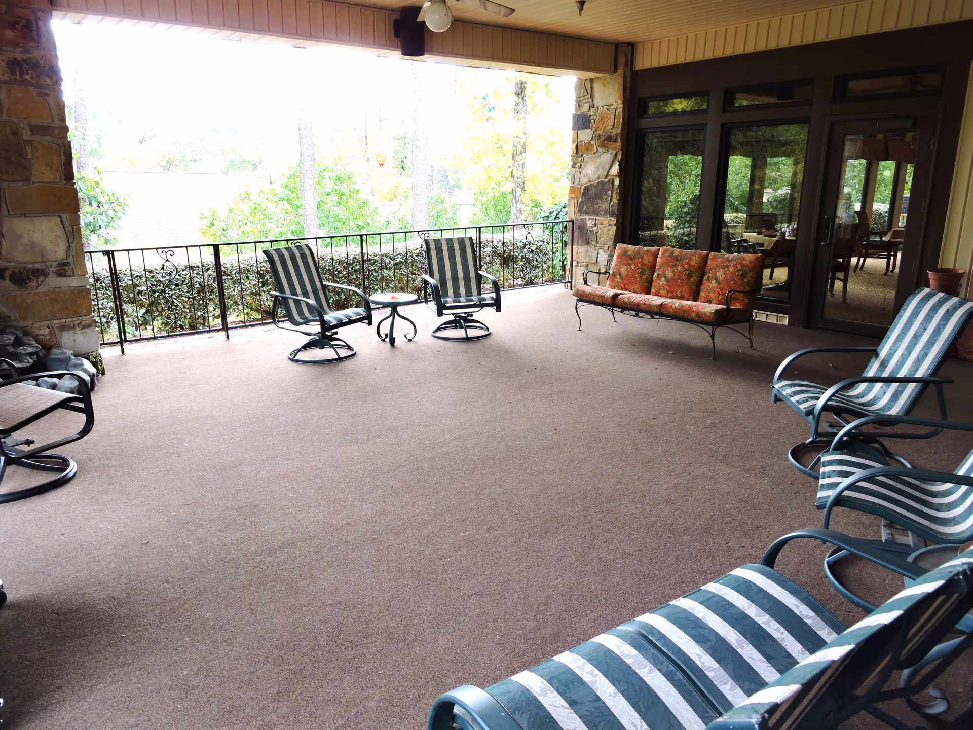 Covered outdoor patio with striped lounge chairs, a floral loveseat and small tables overlooking trees.