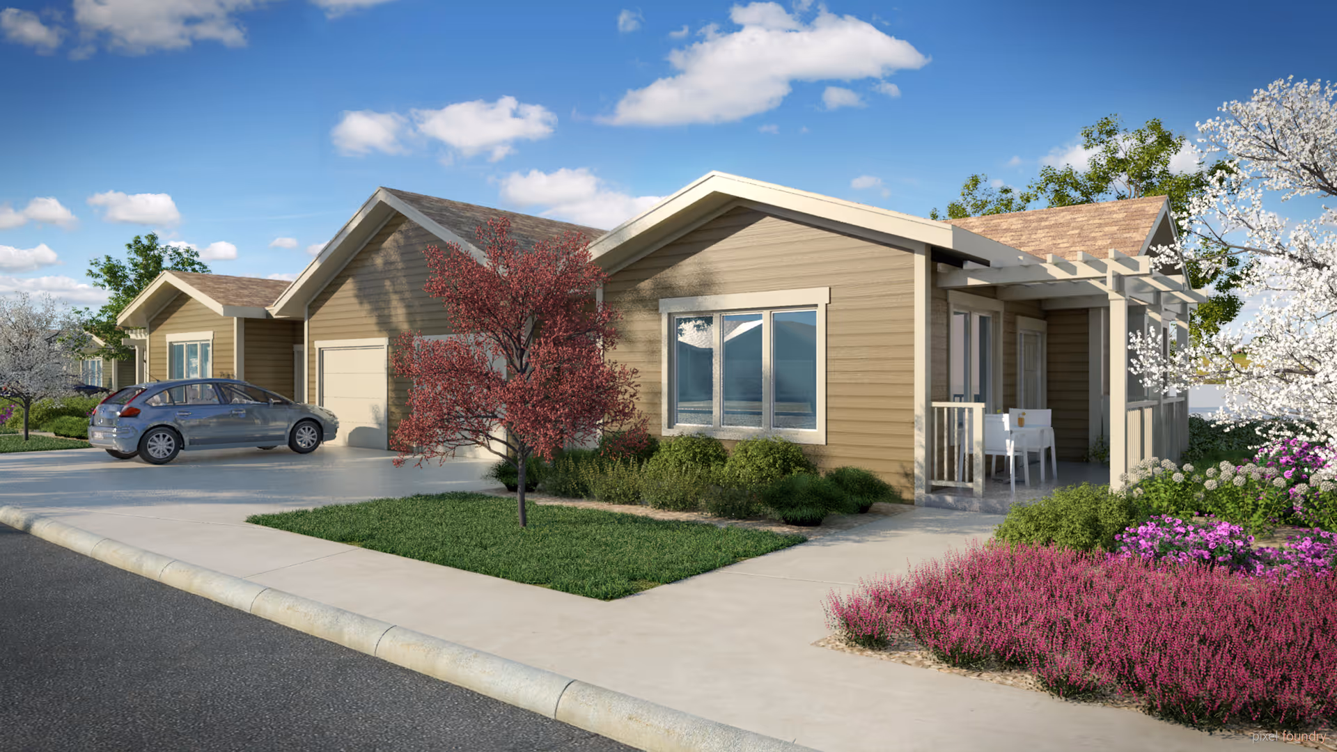 Exterior view of a single-story residential building with beige siding, a small front porch with white chairs, a driveway with a parked car, and landscaped greenery including trees and flowering bushes under a blue sky with scattered clouds.