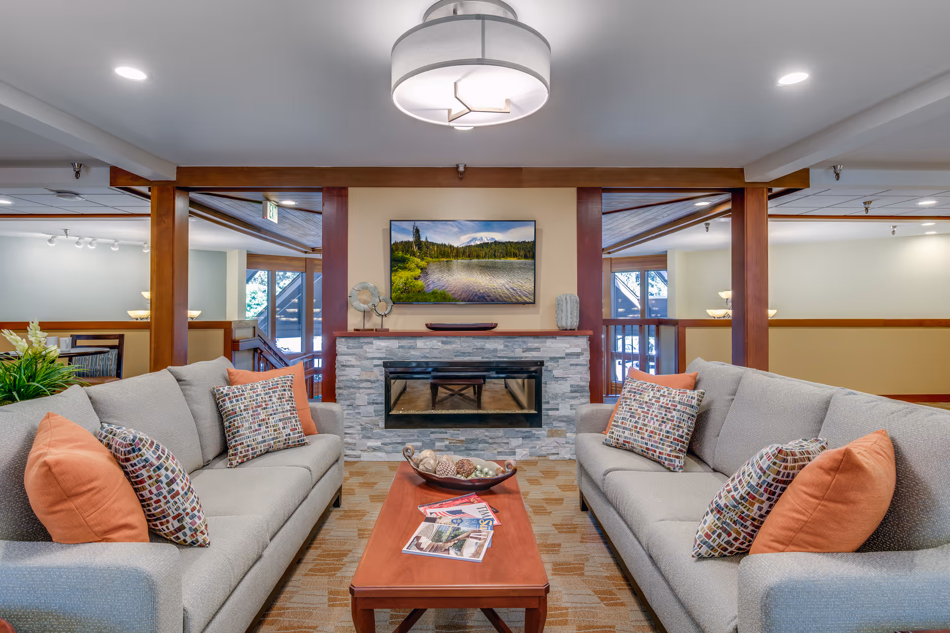 A cozy communal living room with two sofas facing a stone fireplace and a wall-mounted TV above a wooden coffee table.