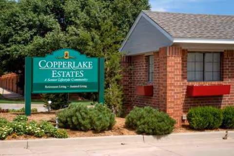 Exterior view of a brick senior living building with a green sign and landscaping.