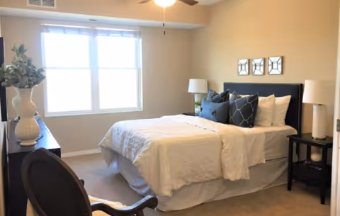 Bright bedroom with a made bed, decorative pillows, bedside tables, and a window letting in natural light.