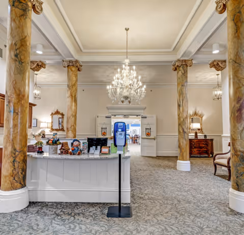 Elegant reception lobby with marble columns, a crystal chandelier, a front desk and a hand sanitizer station.