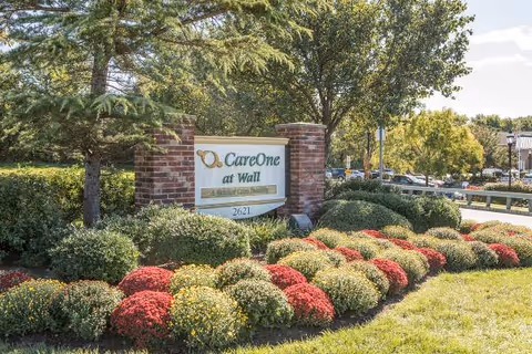 CareOne at Wall sign with brick pillars, surrounded by colorful shrubs and trees.