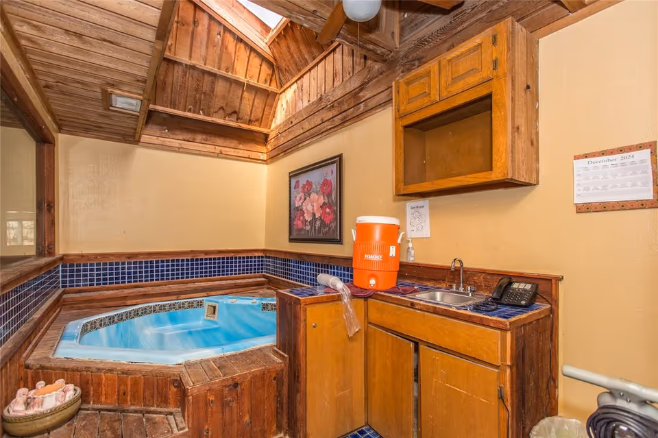 Wood-paneled interior room with a built-in blue hot tub, tiled counter with sink and cabinets, and a skylight above.