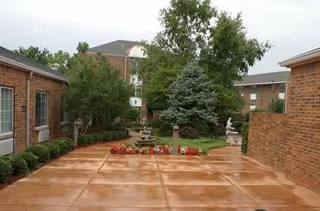 Brick-walled outdoor courtyard with trees, flower beds, and a central fountain.