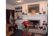 Interior living room showing a white fireplace mantel topped with a mirror and decorations, a vase of red flowers on a coffee table, and holiday figurines.